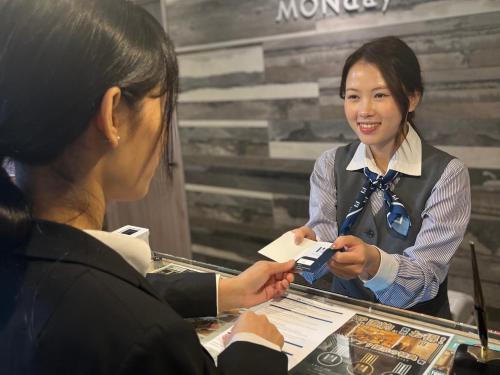 a woman is handing a woman a piece of paper at hotel MONday Haneda Airport in Tokyo