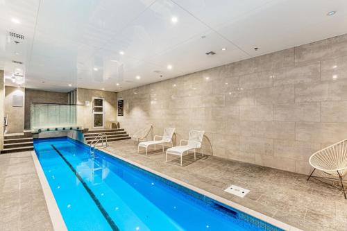 a pool in a hotel with chairs and a table at Stylish Modern Unit w Balcony and Pool Zodiak Stays in Auckland