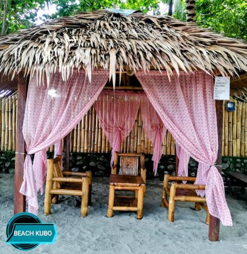 a thatch hut with two chairs and a table at Sevens Hideaway Beach Resort in Siaton