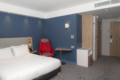 a hotel room with a bed and a red chair at Holiday Inn Express Caen Epron by IHG in Caen