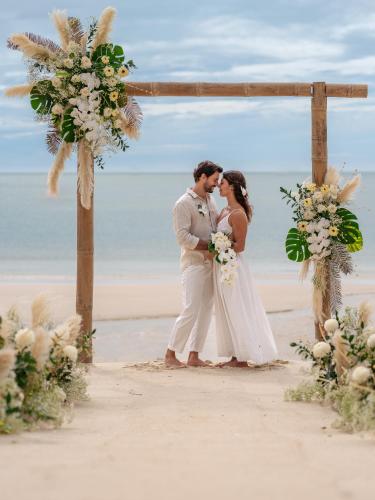 a bride and groom standing under a wedding arch on the beach at Anantara Rasananda Koh Phangan Villas in Thong Nai Pan Noi