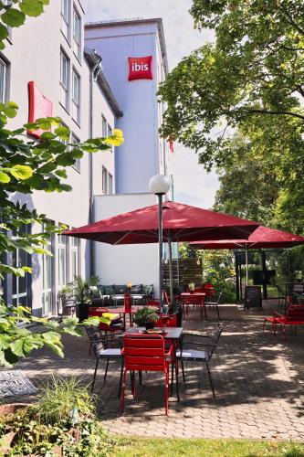 a group of tables and chairs with red umbrellas in front of a building at ibis Hotel Regensburg City in Regensburg