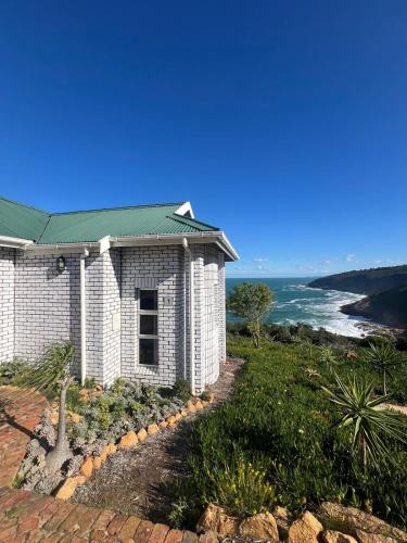 a white building with a green roof next to the ocean at Blue Whale Resort in George