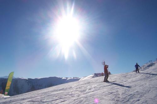 two people standing on a snow covered slope with the sun at Gourmet-Hotel Grünwald in Leogang