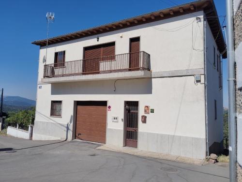 a white building with a brown door and a balcony at La Fuente de la Covatilla in La Hoya