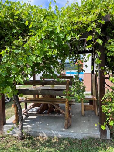 a wooden bench under an arch with green trees at Dedina kuća in Gornji Milanovac