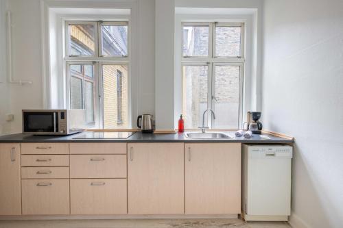 a kitchen with a sink and a microwave and two windows at Super Central 2BR Apartment in Old Town Copenhagen in Copenhagen
