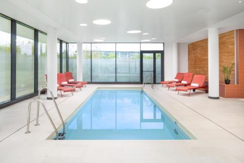 a pool with red chairs in a large room with windows at Hyatt Place Paris Charles de Gaulle Airport in Roissy-en-France