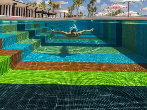 a man swimming in a pool with a colorful floor at SO/ Maldives in South Male Atoll