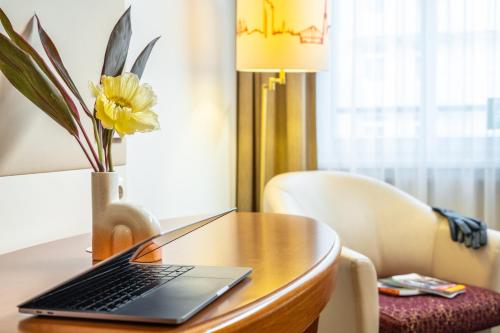 a laptop on a wooden table with a vase of flowers at Hotel Mercure Wien Westbahnhof in Vienna