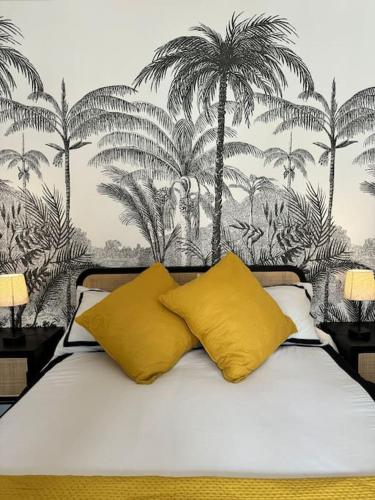 un lit avec deux oreillers jaunes et des palmiers dans l'établissement 2 Pièces Parisien à Proximité de la Défense, à Puteaux