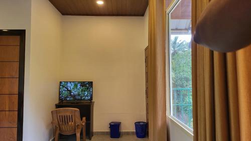 Zimmer mit einem TV, einem Stuhl und einem Fenster in der Unterkunft Green Cradle in Munnar