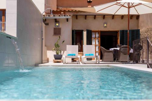 a swimming pool with chairs and an umbrella next to a house at Can Olivera in Llubí