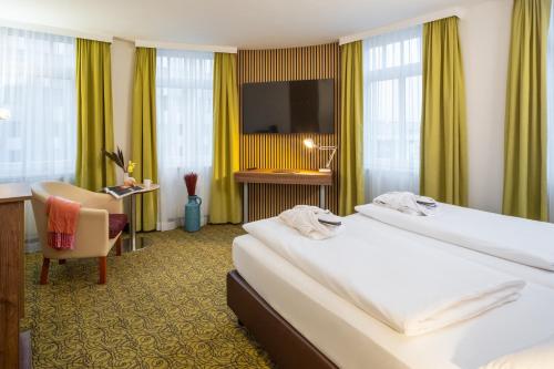 a hotel room with two beds and a desk and a television at Hotel Mercure Wien Westbahnhof in Vienna