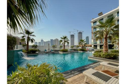 a large swimming pool with palm trees and a building at HAVN - Smart Home Studio in Oxford Terraces, JVC in Dubai