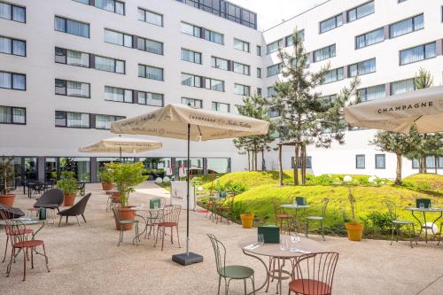 a patio with tables and chairs and umbrellas in front of a building at Hyatt House Paris Charles de Gaulle Airport in Roissy-en-France