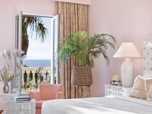a bedroom with a bed and a plant in front of a window at Mandola Rosa at Riviera Olympia, A Grecotel Resort to Live in Loutra Killinis