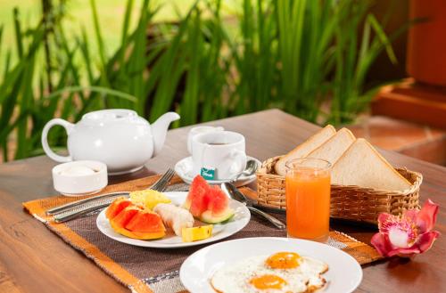 a table with plates of breakfast food and a cup of orange juice at Ging Oya Lodge in Waikkal