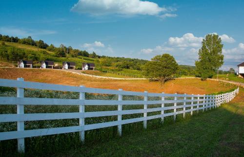a white fence in front of a field with houses at Family Resort Plitvice Lakes in Rastovača