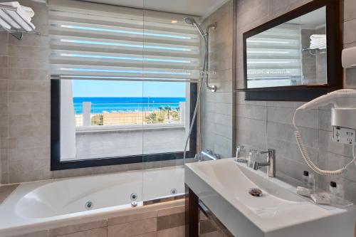 Un baño con bañera, lavabo y ventana. en Nozha Beach Resort & Spa, en Hammamet