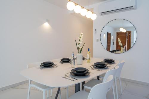 a white dining room with a white table and a mirror at Luxury brand new holiday apartments TOP location in Is-Swieqi