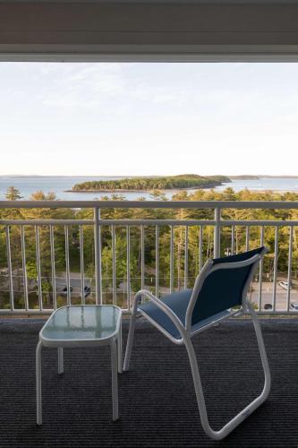 a chair and a stool on a balcony with the ocean at Bluenose Inn - Bar Harbor Hotel in Bar Harbor