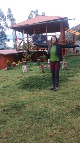 a woman standing in the grass in front of a building at the wooden house choquequirao in Cachora