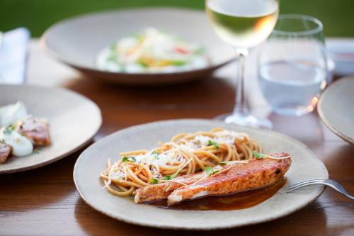 a plate of pasta with a fish and a glass of wine at Ikos Dassia in Dassia