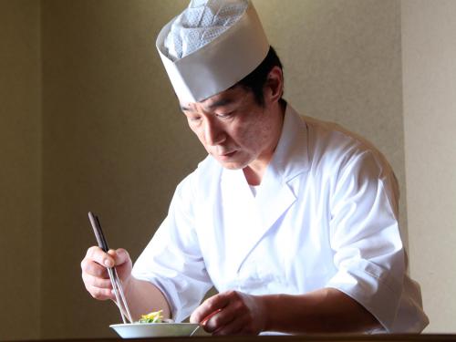 a man in a chefs hat eating a bowl of food at Hotel Tsubakino in Yamanouchi