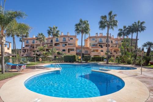 a swimming pool in front of a building with palm trees at Spacious duplex apartment families and couples in Manilva