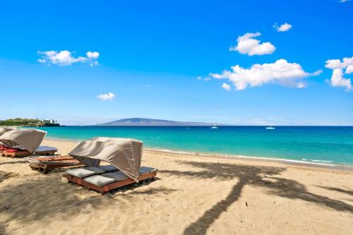 two lounge chairs and umbrellas on a beach at Aston Maui Kaanapali Villas in Lahaina