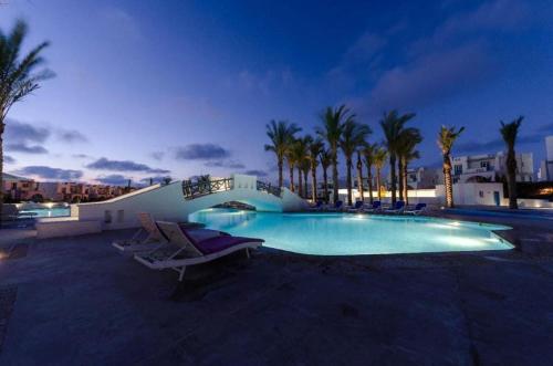 a swimming pool with chairs and palm trees at night at Chalet in Mountain View ras elhekma in Ras Elhekma