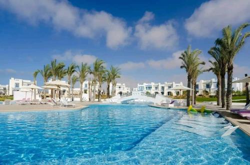 a large swimming pool with palm trees and buildings at Chalet in Mountain View ras elhekma in Ras Elhekma