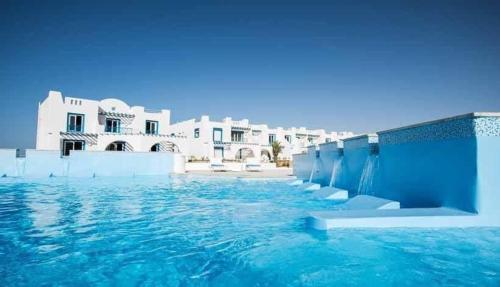 a swimming pool with blue water and white buildings at Chalet in Mountain View ras elhekma in Ras Elhekma