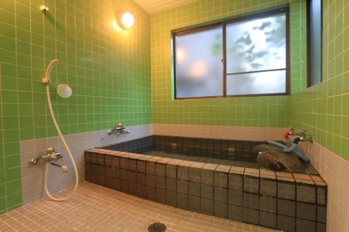屋久島にある民宿　宮之浦荘の緑のタイル張りのバスルーム(窓のあるバスタブ付)