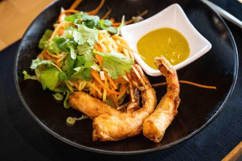 a black plate with shrimp and a salad and dipping sauce at Logis Hôtels Gnàc é Pause in Saint-Lon-les-Mines