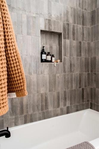 a bathroom with a gray tiled shower with three bottles on a shelf at The Gable - 3 BLKS from Main St in Fredericksburg