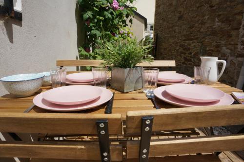 une table en bois avec des assiettes et des verres roses dans l'établissement Ma petite maison bretonne, à Guimiliau