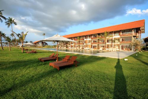 a building with two benches and an umbrella in the grass at Anantaya Resort & Spa Chilaw in Chilaw