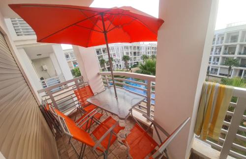 a table and chairs on a balcony with a red umbrella at superbe appartement vue piscine in Bouznika