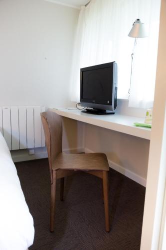 a room with a desk with a tv and a chair at Hotel inn Design Laval in Laval