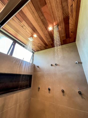 a bathroom with a shower with water pouring from a ceiling at Casa com piscina aquecida, cozinheira, 30m do mar in Barra do Camaragibe