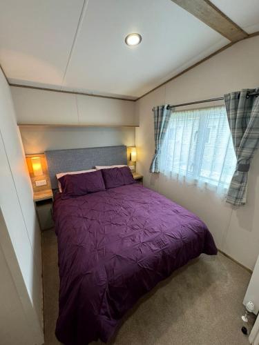 a purple bed in a small room with a window at Golden Palm Resort - The Blenheim Retreat - Coastal Caravan Breaks in Chapel Saint Leonards
