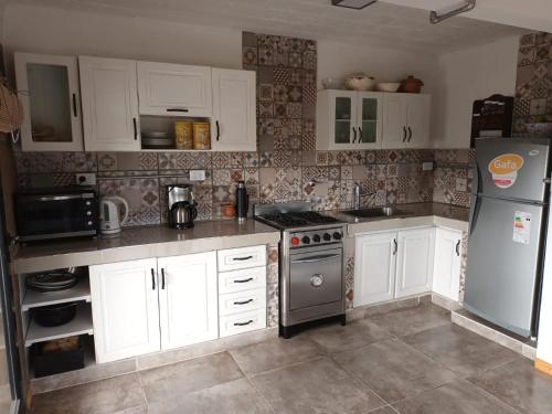 Una cocina con gabinetes blancos y un refrigerador de acero inoxidable. en Siu Kiu - Casa de Montaña, en El Parador