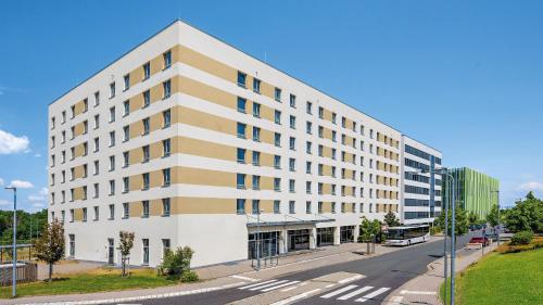 a large white building on a street with a road at Hey Lou Hotel Frankfurt Airport in Kelsterbach