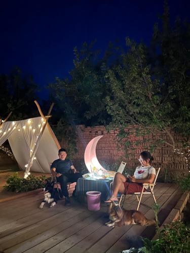 two people sitting on a deck at night with their dogs at 达卜·九宿民宿 in Turfan