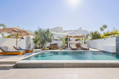 a pool with chairs and umbrellas next to a house at Kouros Exclusive Hotel & Suites - Adults Only in Faliraki