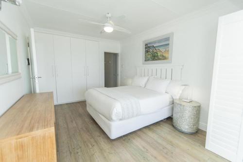 a white bedroom with a bed and a ceiling fan at Luxury On The Beach in Summerstrand
