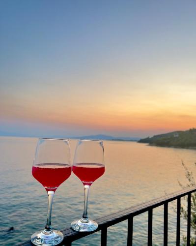 two glasses of red wine sitting on a balcony overlooking the water at Sunset of Pelion in Kato Gatzea