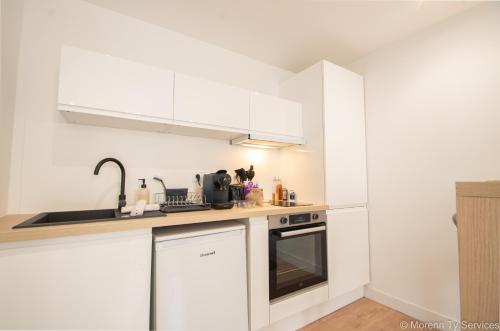 une cuisine avec des armoires blanches, un évier et une cuisinière dans l'établissement Studio calme proche Vilaine - Ty ar Sant-Elier, à Rennes